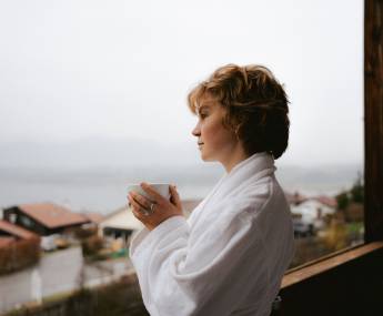 A woman holding a cup of herbal tea enjoys a day of relaxation on the terrace overlooking Lake Hopfensee